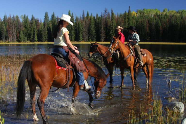group of friends riding horses near lake